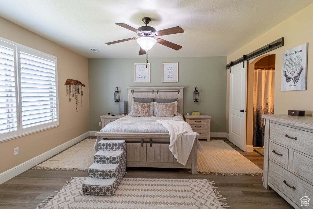 Bedroom featuring a barn door, dark wood-style flooring, and ceiling fan