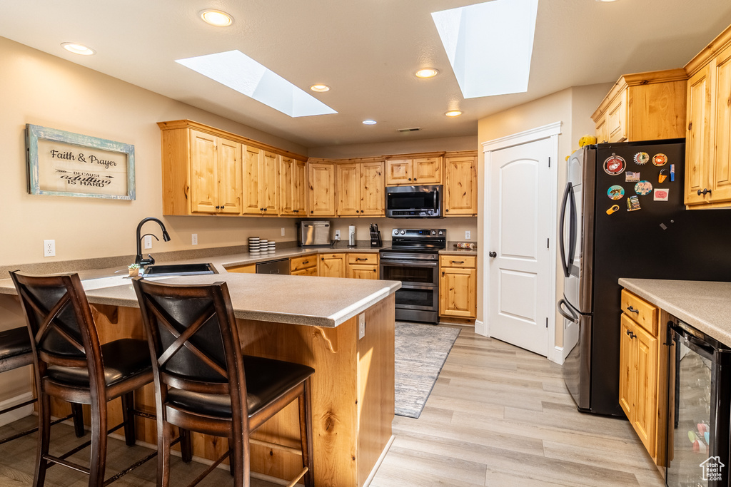 Kitchen featuring stainless steel appliances, a skylight, wine cooler, a peninsula, and a kitchen bar