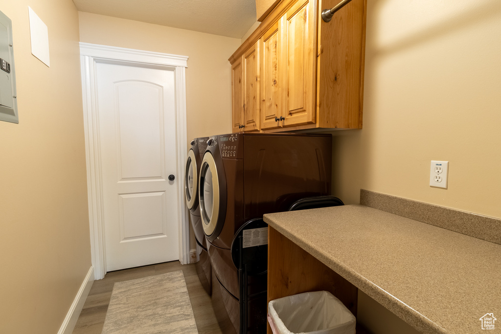 Washroom featuring independent washer and dryer, cabinet space, light wood-style floors, and electric panel