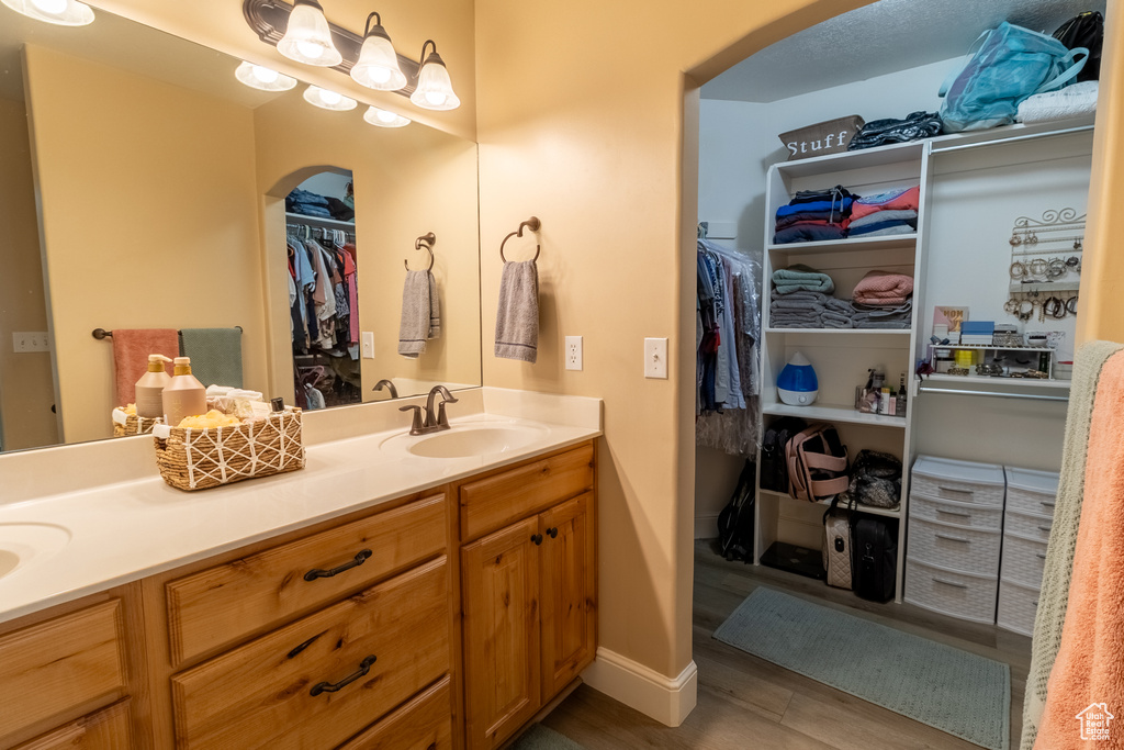 Bathroom with double vanity, a walk in closet, and wood finished floors