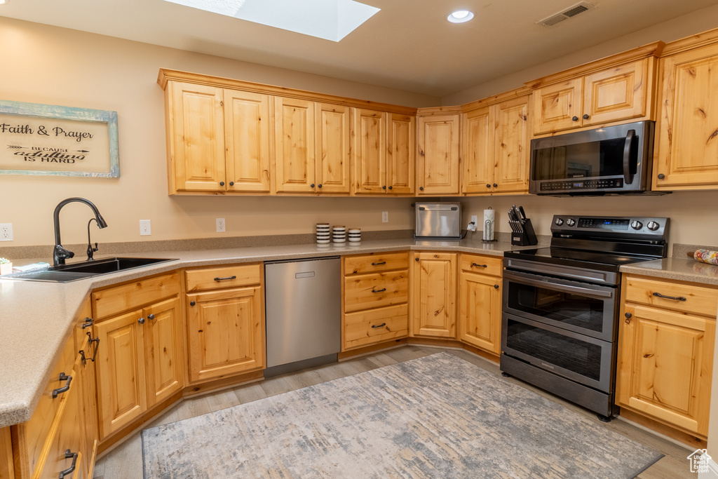Kitchen featuring stainless steel appliances, a skylight, light brown cabinetry, light wood-style flooring, and recessed lighting