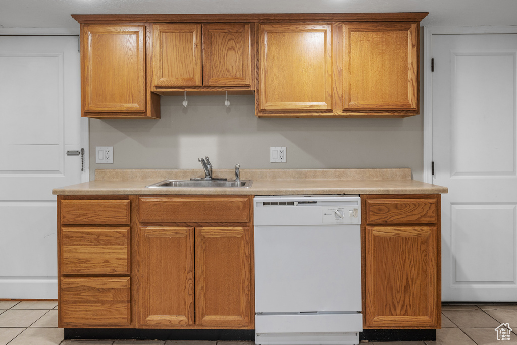 Kitchen featuring white dishwasher, light tile patterned floors, light countertops, and brown cabinets