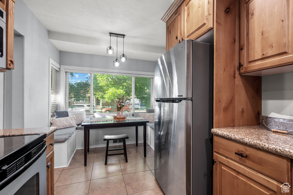 Kitchen featuring appliances with stainless steel finishes, light stone counters, light tile patterned floors, decorative light fixtures, and brown cabinetry
