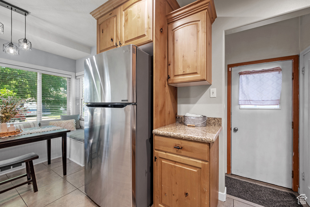 Kitchen with freestanding refrigerator, light stone counters, light tile patterned floors, light brown cabinetry, and hanging light fixtures