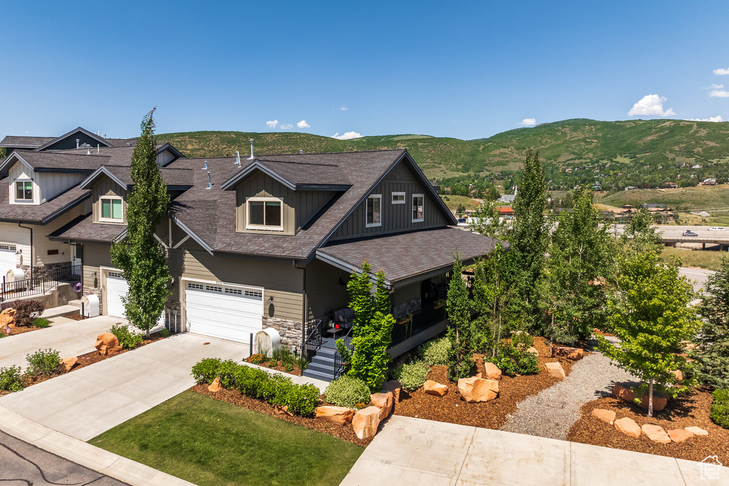 Craftsman house with roof with shingles, concrete driveway, a mountain view, a garage, and stone siding