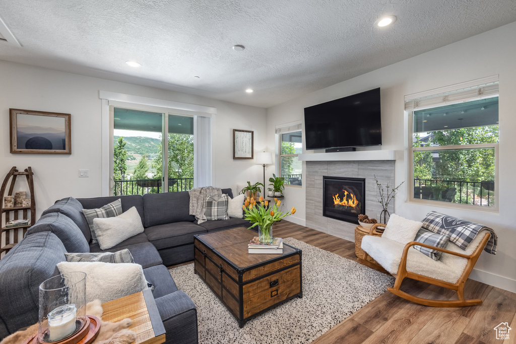 Living room with wood finished floors, a textured ceiling, a tiled fireplace, and recessed lighting