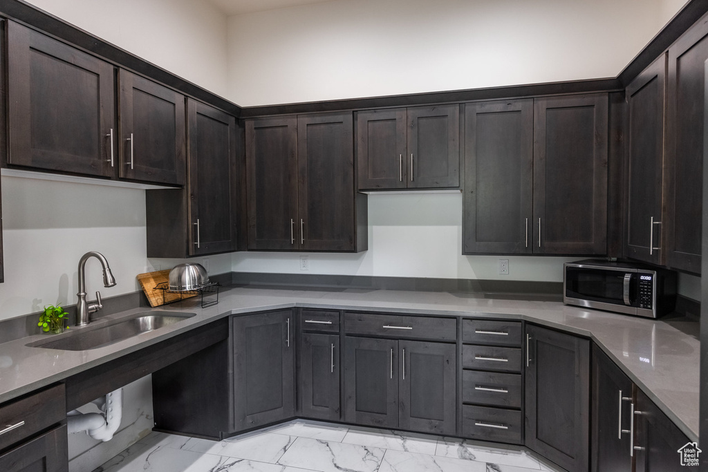 Kitchen featuring stainless steel microwave, light marble finish floors, and dark brown cabinetry