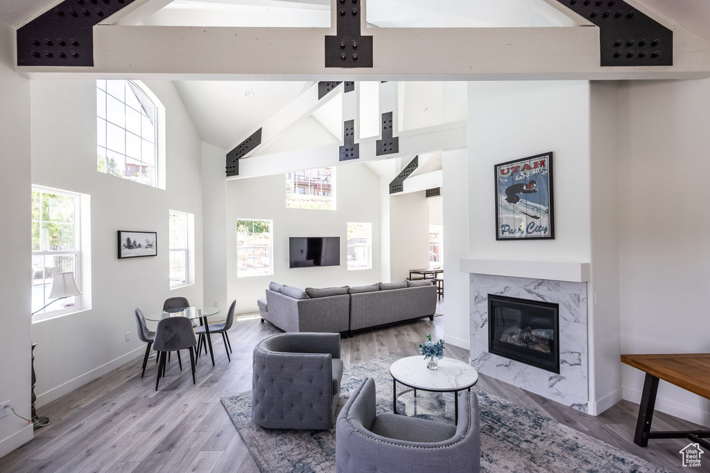Living area with light wood-style floors, high vaulted ceiling, a high end fireplace, and beam ceiling