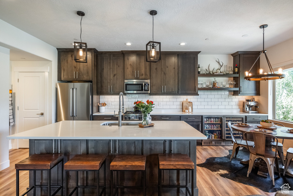 Kitchen featuring appliances with stainless steel finishes, light wood-type flooring, dark brown cabinetry, open shelves, and recessed lighting