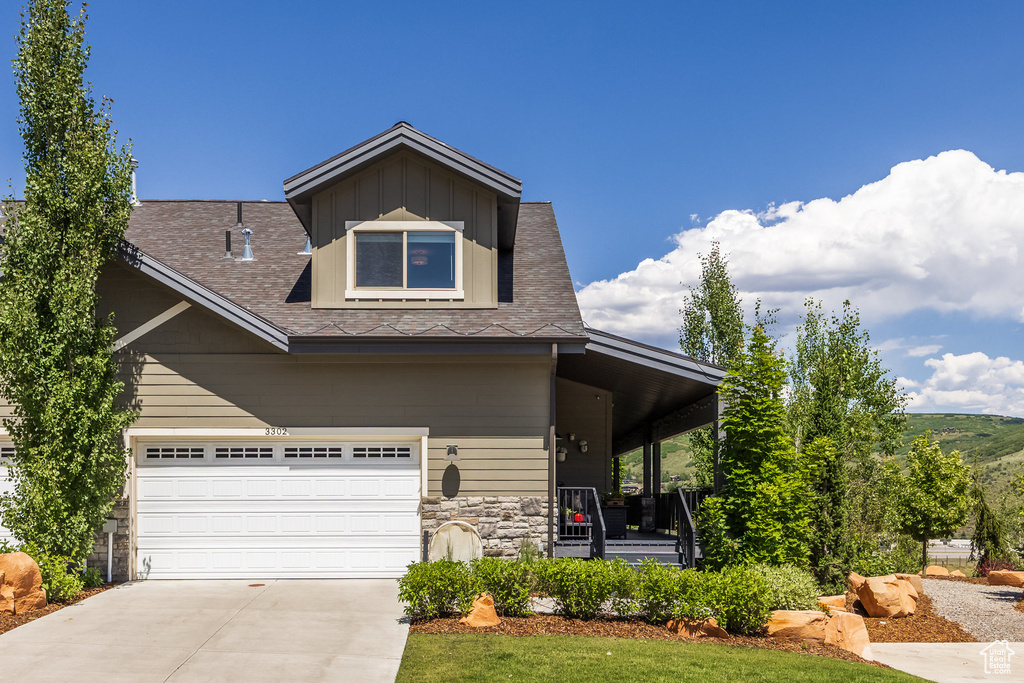 View of front of home with a porch, stone siding, concrete driveway, and roof with shingles