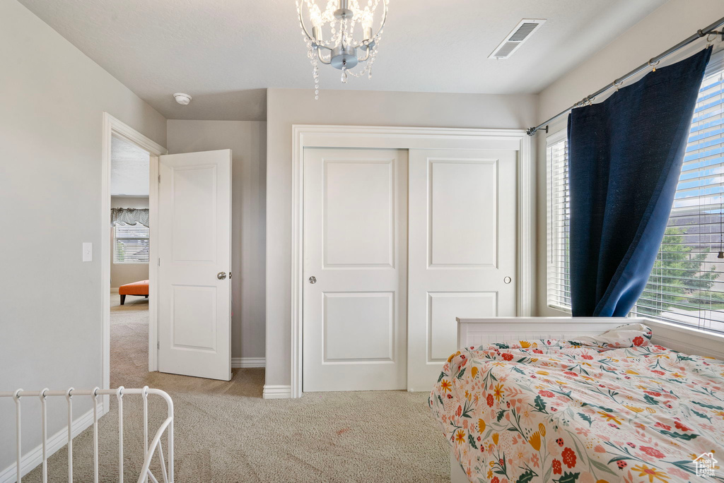Bedroom featuring light colored carpet, multiple windows, a closet, and a chandelier