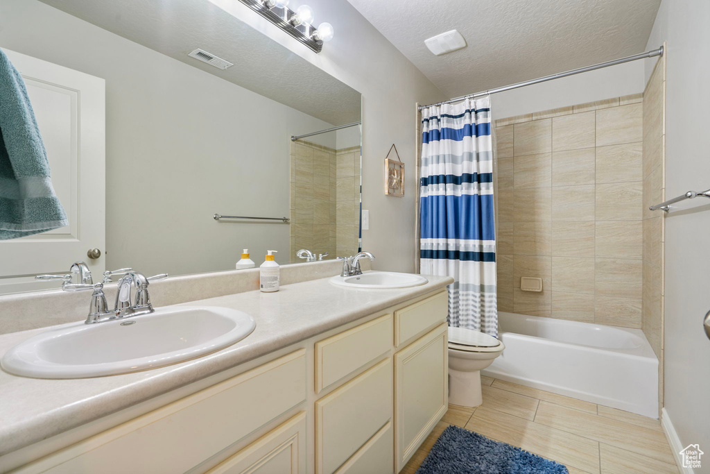 Full bathroom with double vanity, shower / tub combo with curtain, tile patterned flooring, and a textured ceiling