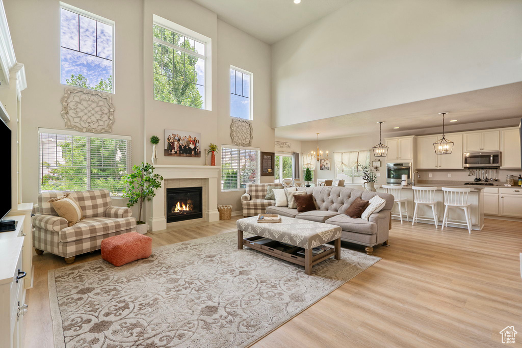 Living area with light wood-style floors, a glass covered fireplace, a towering ceiling, recessed lighting, and a chandelier
