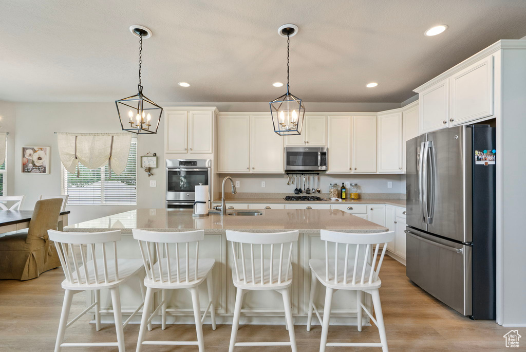 Kitchen with stainless steel appliances, light countertops, light wood-type flooring, white cabinets, and decorative light fixtures