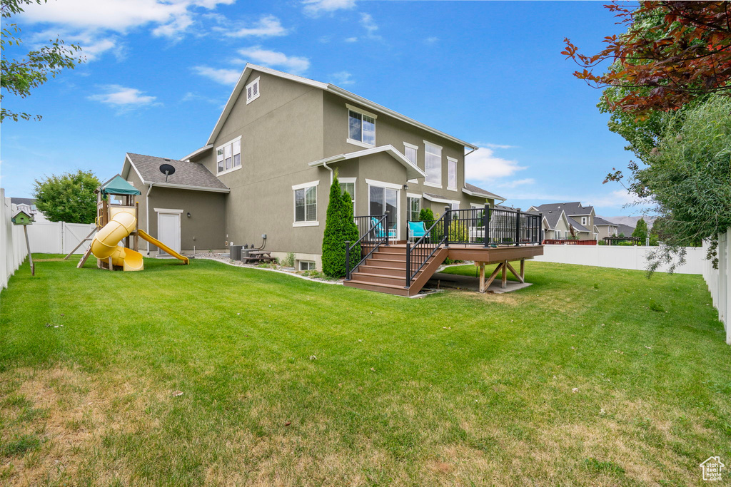 Back of house with a fenced backyard, a playground, a wooden deck, stucco siding, and stairs