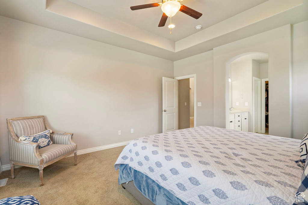 Bedroom with arched walkways, a raised ceiling, and light carpet