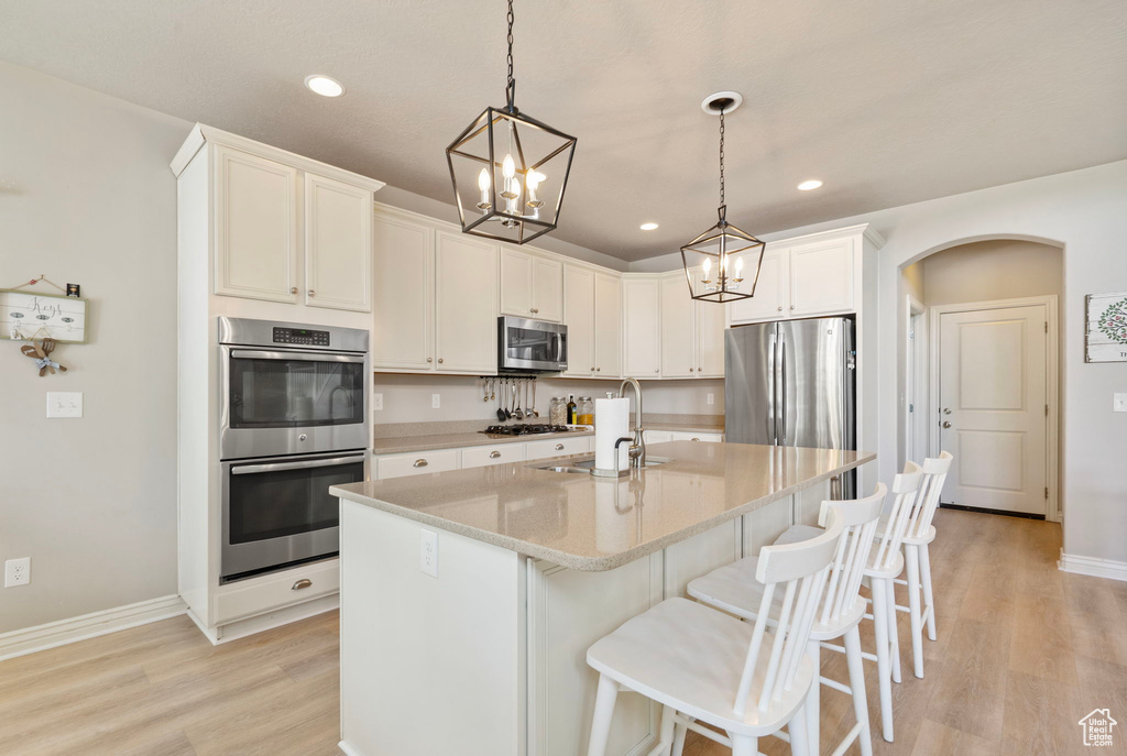Kitchen with appliances with stainless steel finishes, a chandelier, light wood-style flooring, arched walkways, and a breakfast bar