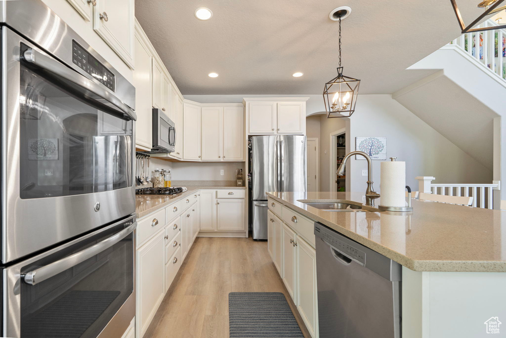 Kitchen with appliances with stainless steel finishes, light wood-style floors, recessed lighting, decorative light fixtures, and a center island with sink