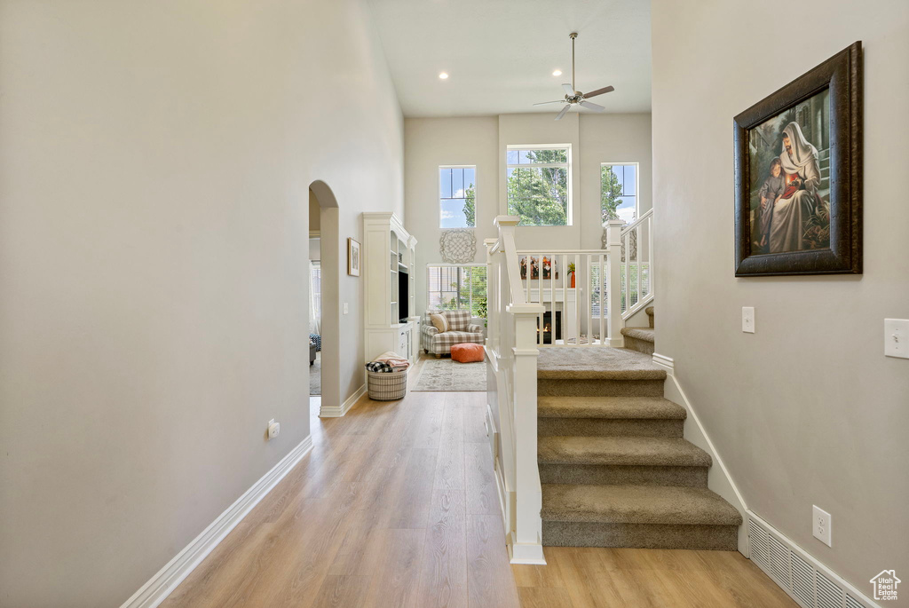 Stairs featuring arched walkways, ceiling fan, wood finished floors, recessed lighting, and a high ceiling
