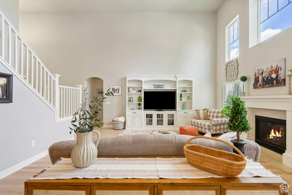 Living room with a high ceiling, a glass covered fireplace, light wood finished floors, stairway, and arched walkways