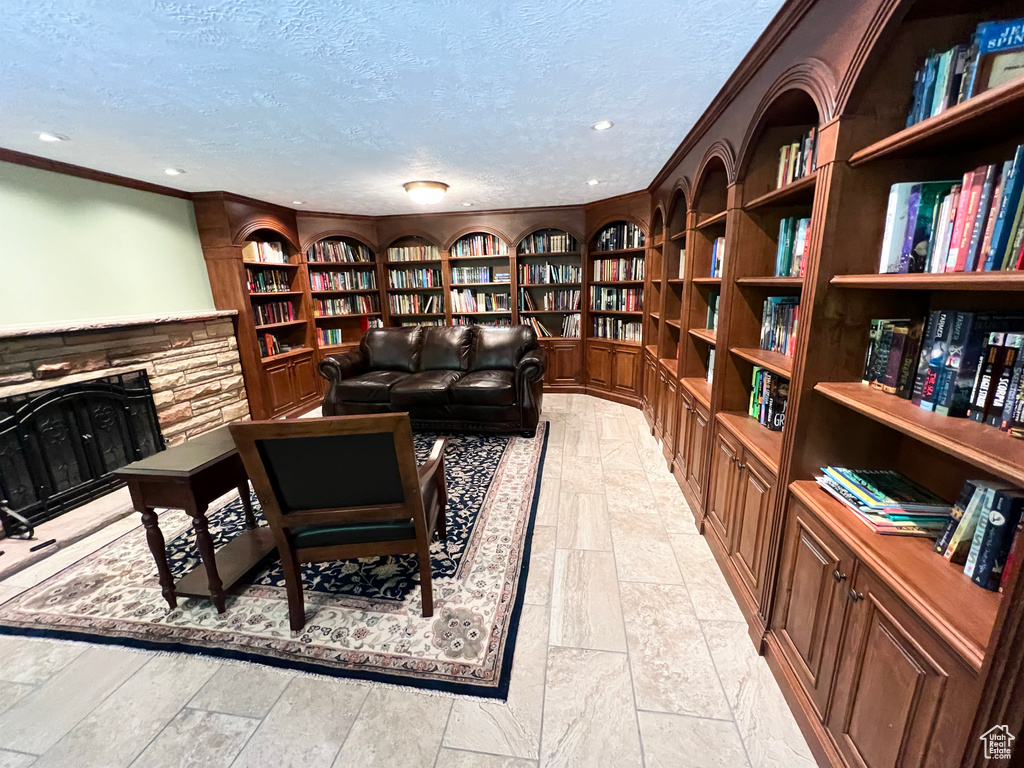 Living area with bookshelves, a textured ceiling, built in shelves, crown molding, and a stone fireplace