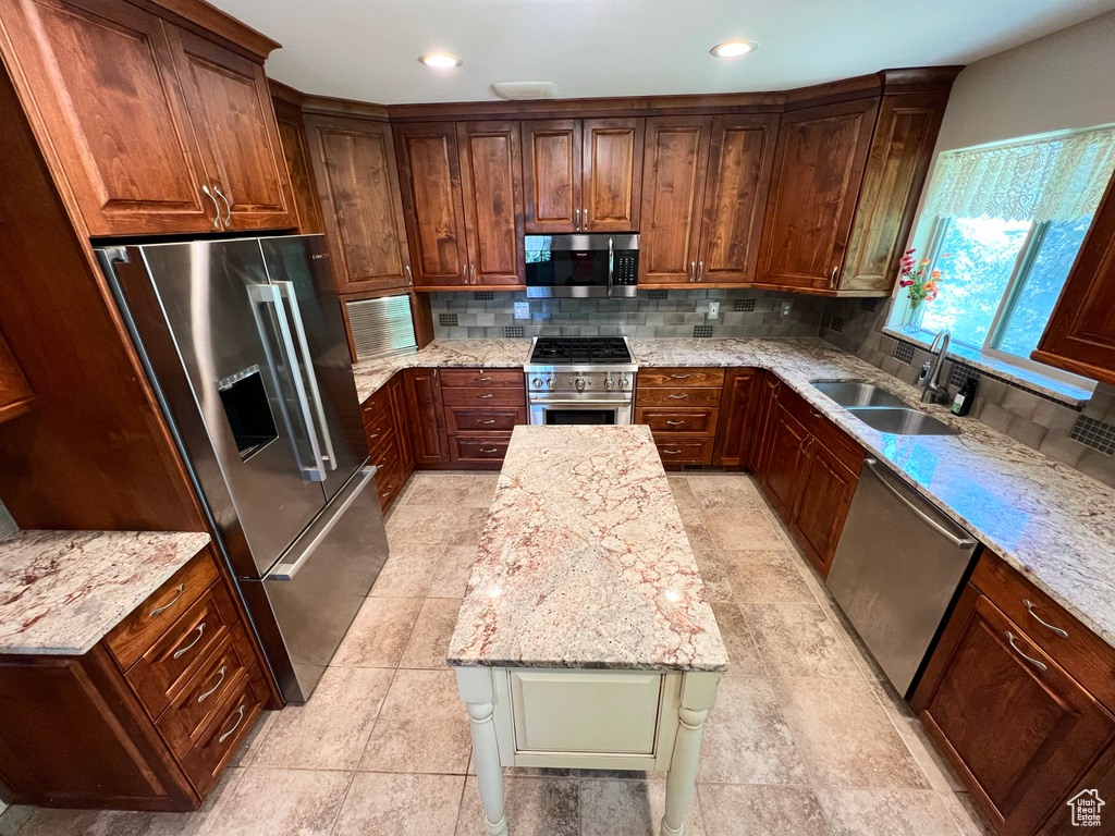 Kitchen featuring high end appliances, backsplash, light stone countertops, recessed lighting, and a kitchen island