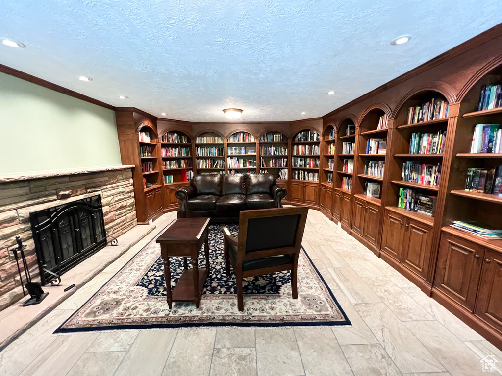 Living area with bookshelves, built in shelves, ornamental molding, recessed lighting, and a stone fireplace