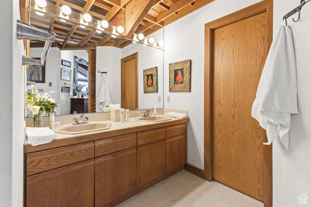 Full bath featuring double vanity, tile patterned flooring, and beamed ceiling