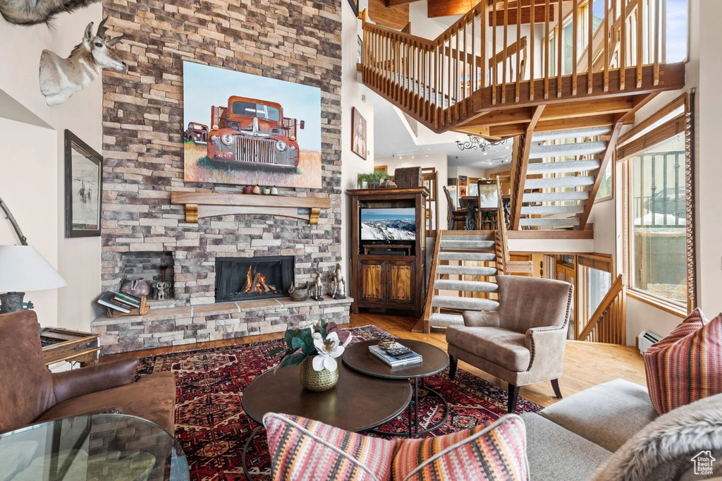 Living area featuring wood finished floors, a towering ceiling, stairs, and a stone fireplace