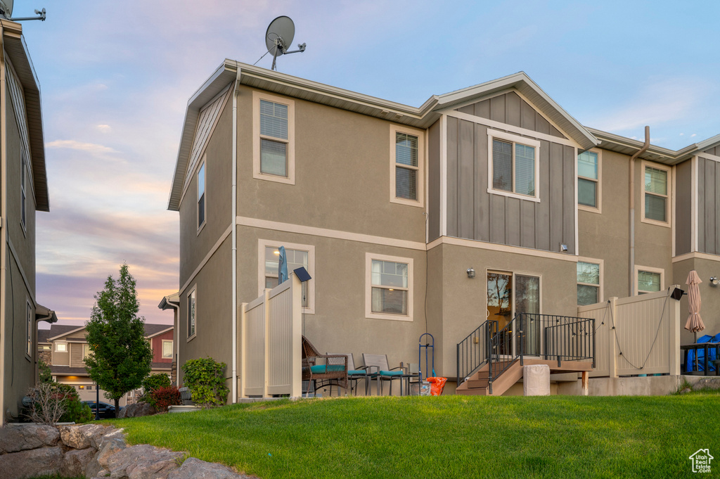 Back of house at dusk featuring board and batten siding, a yard, and stucco siding