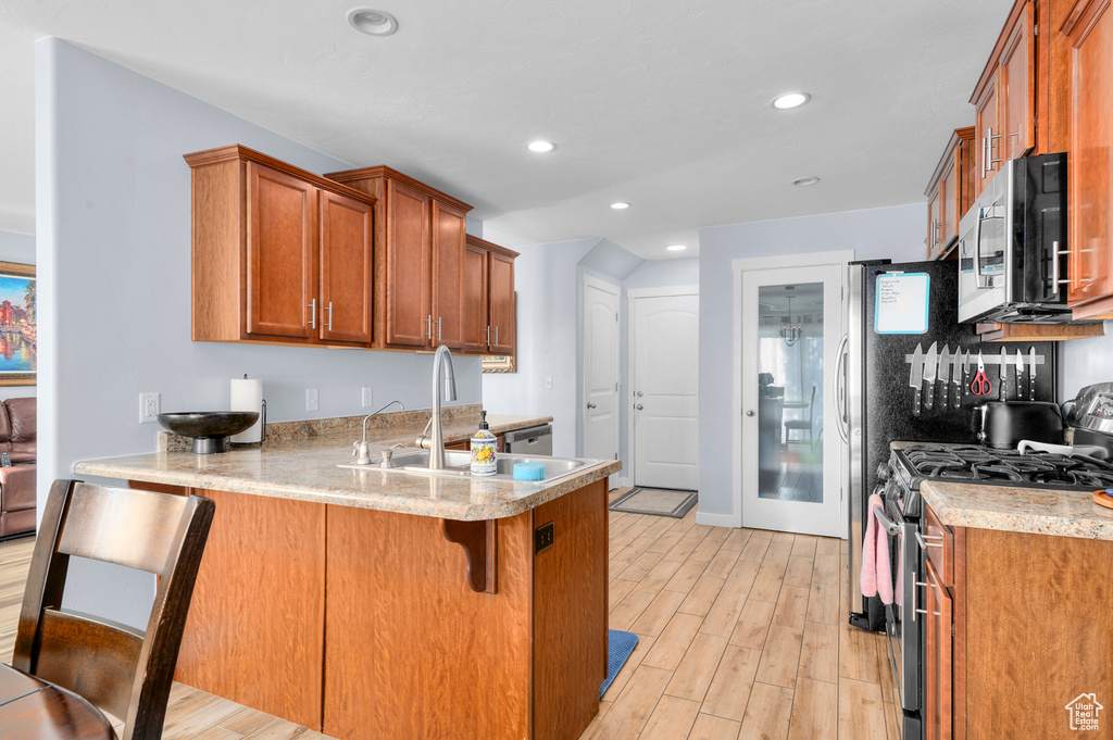Kitchen with stainless steel appliances, brown cabinetry, a peninsula, light wood-type flooring, and recessed lighting
