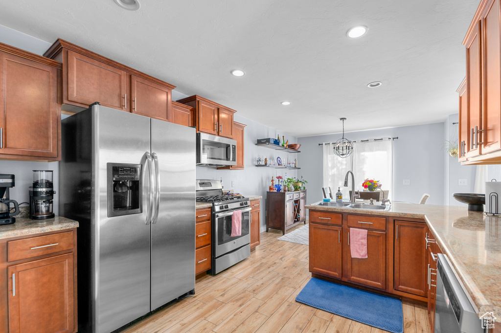 Kitchen with appliances with stainless steel finishes, a peninsula, light wood-style flooring, brown cabinetry, and recessed lighting