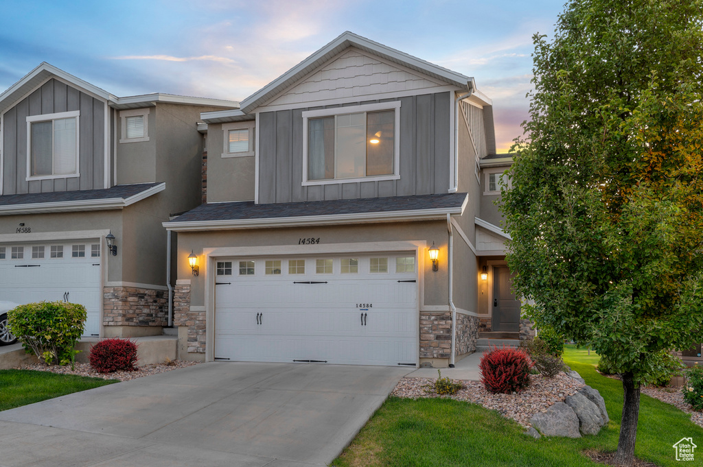View of front facade featuring board and batten siding, stone siding, an attached garage, driveway, and stucco siding