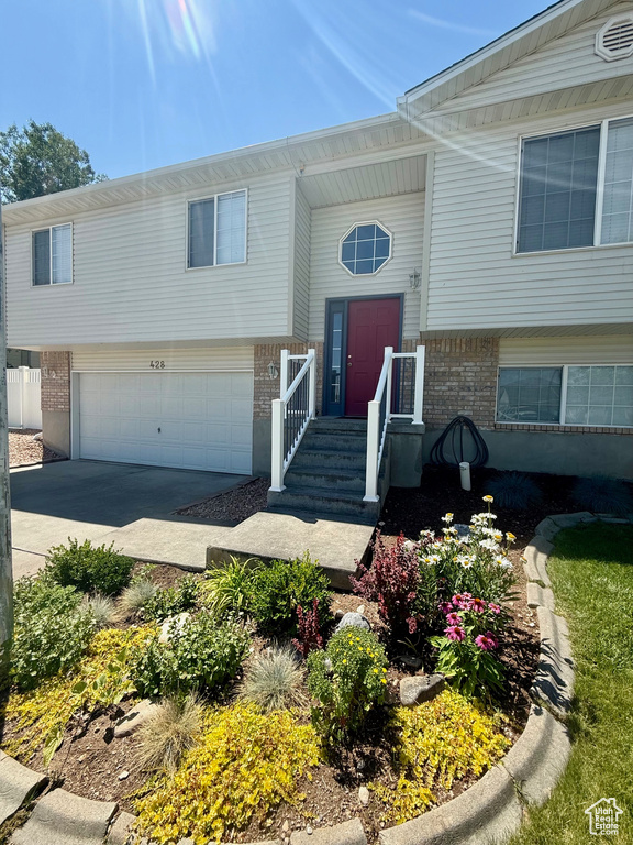 Raised ranch featuring brick siding, an attached garage, and concrete driveway