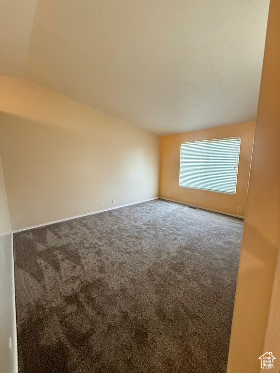 Carpeted spare room featuring lofted ceiling and baseboards