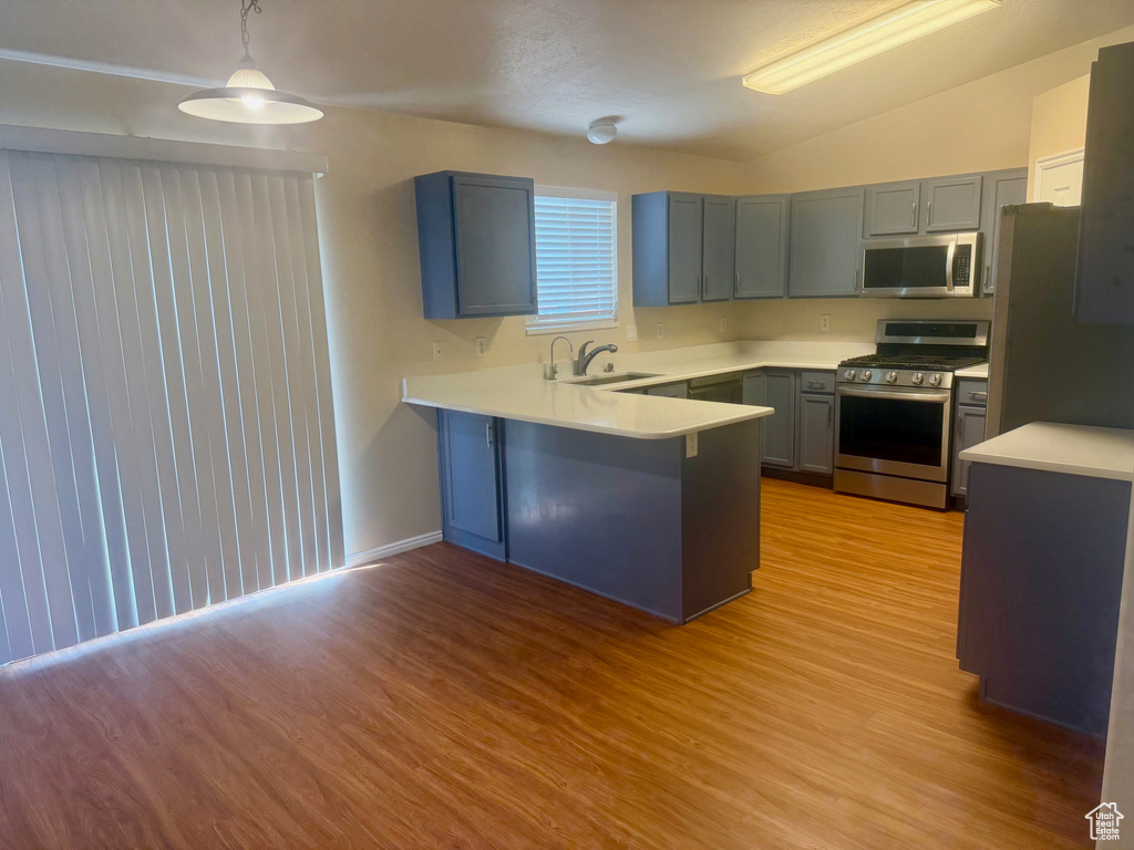 Kitchen with appliances with stainless steel finishes, a peninsula, light wood-type flooring, lofted ceiling, and light countertops