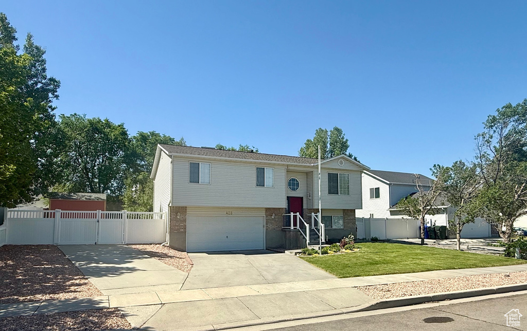 Split foyer home featuring brick siding, driveway, a garage, and a gate