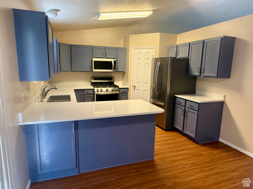 Kitchen featuring appliances with stainless steel finishes, a peninsula, wood finished floors, light countertops, and lofted ceiling