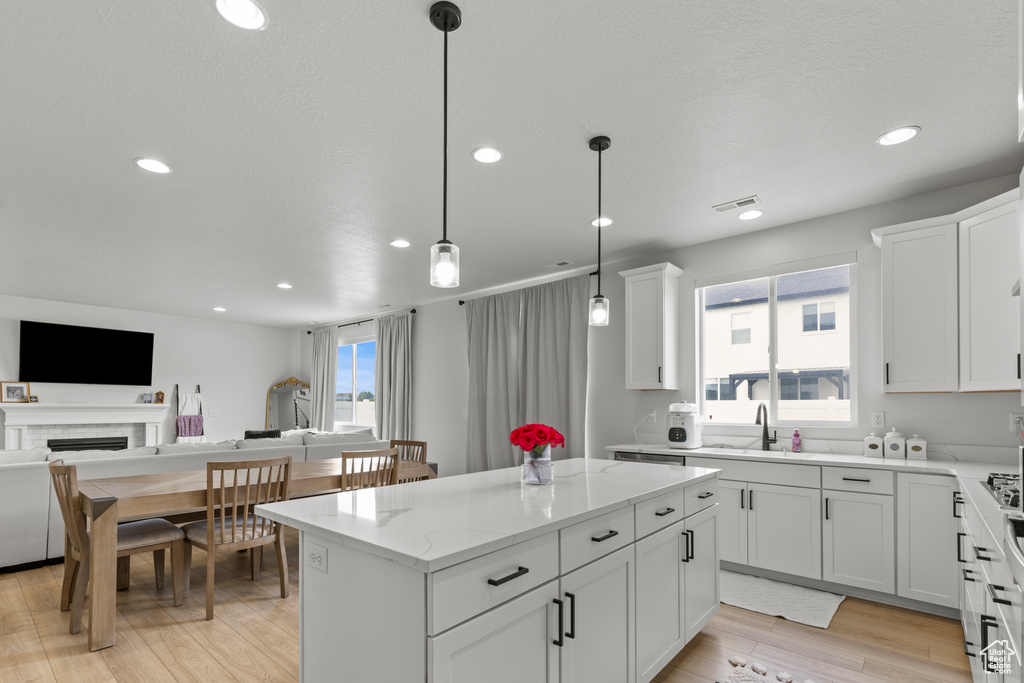 Kitchen with open floor plan, a center island, recessed lighting, light stone counters, and light wood-type flooring