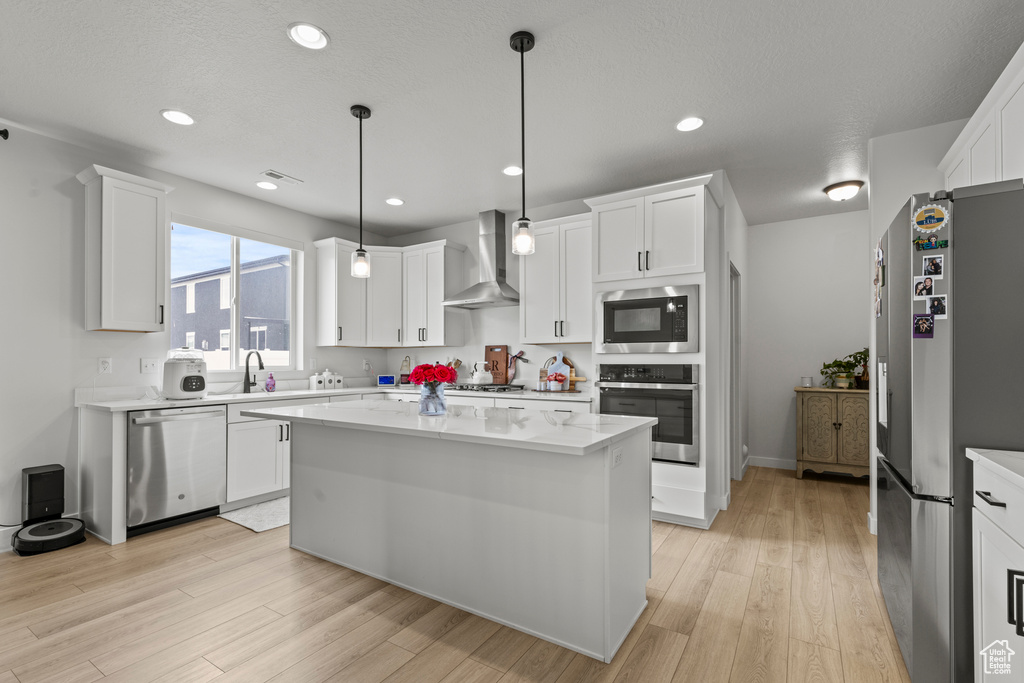 Kitchen with stainless steel appliances, wall chimney range hood, light countertops, light wood-type flooring, and recessed lighting