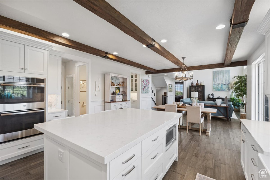 Kitchen with stainless steel appliances, a chandelier, beam ceiling, light countertops, and plenty of natural light
