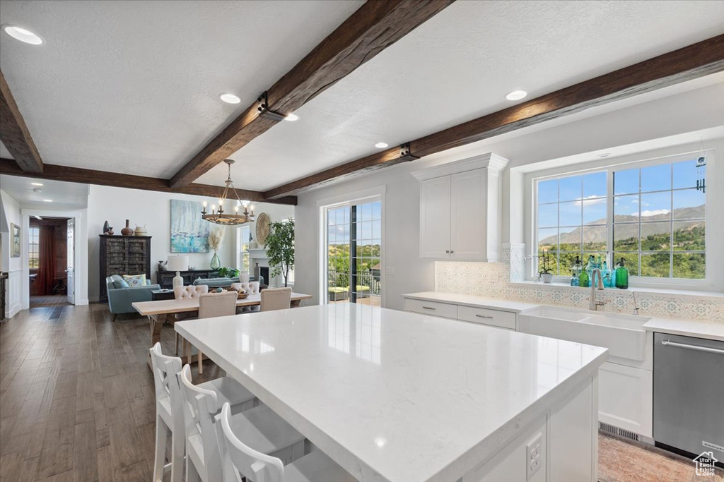Kitchen with stainless steel dishwasher, beam ceiling, a chandelier, light countertops, and white cabinets