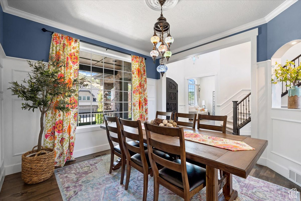 Dining space with crown molding, wood finished floors, arched walkways, stairs, and a textured ceiling