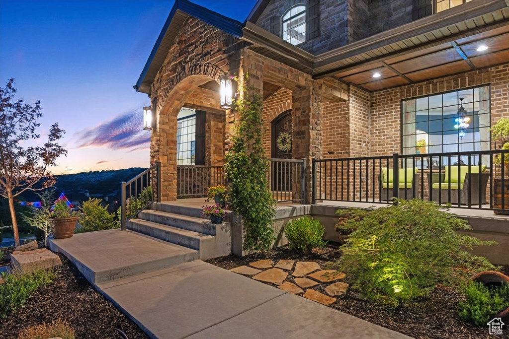 Exterior entry at dusk with covered porch, brick siding, and stone siding