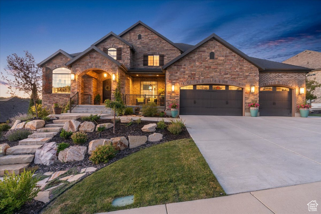 View of front of home with a garage, covered porch, driveway, and stone siding