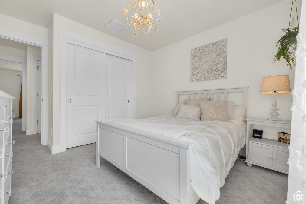 Bedroom with light colored carpet, a chandelier, and a closet
