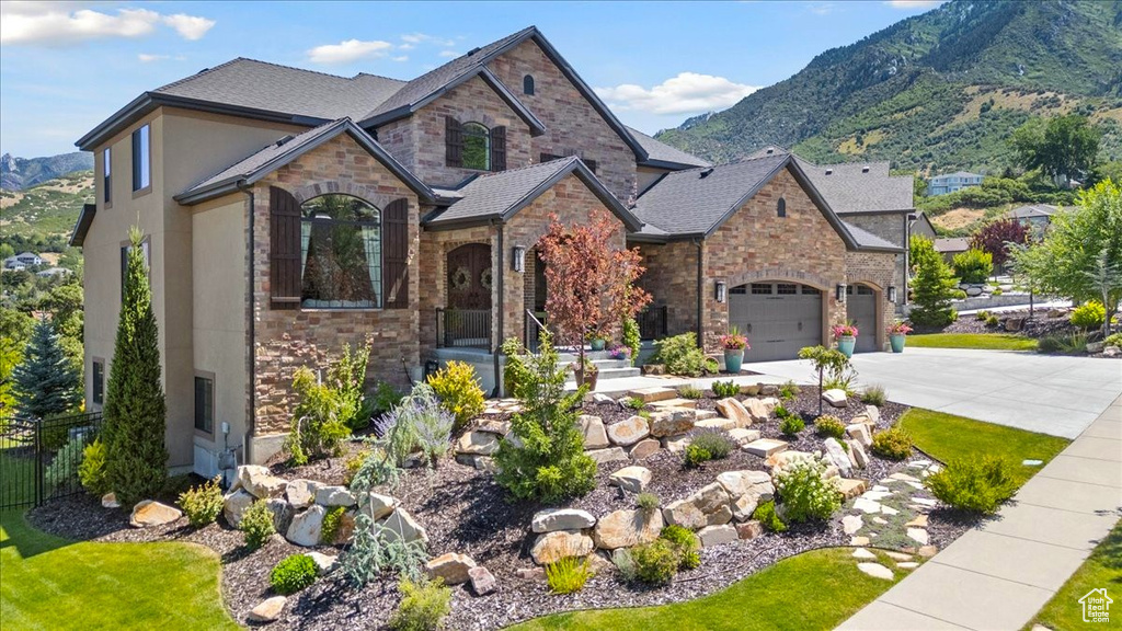 French country inspired facade with stone siding, concrete driveway, a mountain view, and stucco siding