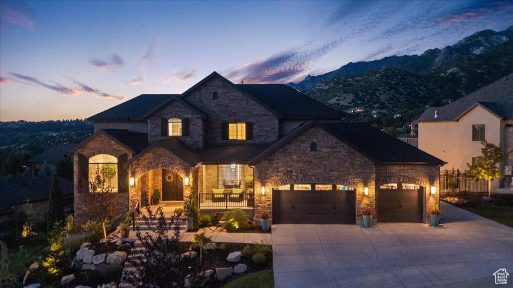 French country inspired facade featuring stone siding, concrete driveway, a mountain view, a porch, and a garage