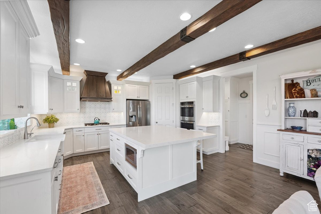 Kitchen featuring custom exhaust hood, appliances with stainless steel finishes, beam ceiling, tasteful backsplash, and white cabinets