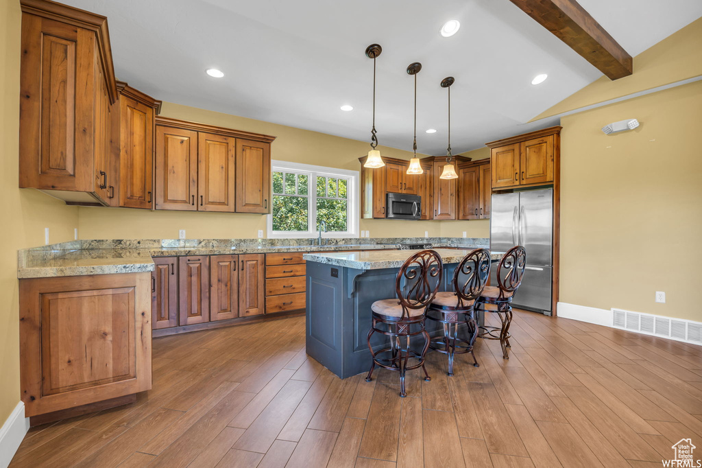 Kitchen featuring stainless steel appliances, brown cabinetry, a kitchen bar, beam ceiling, and a kitchen island
